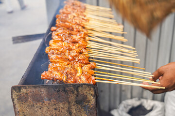Chicken satay grilled over traditional charcoal fire. skewers of meat burn with smoke and...