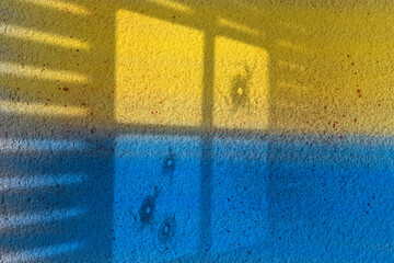 Bloody war, ukrainian colors on a roughcast wall with the shadow of a window with bullet holes in...