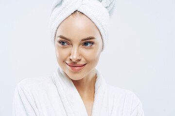 Day spa, beauty and freshness concept. Pensive European woman with healthy skin concentrated aside thoughtfully, feels refreshed after bath procedures, dressed in dressing gown, towel on head