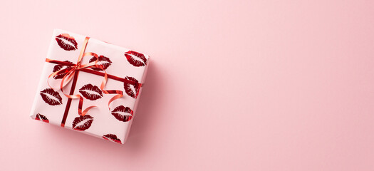 Valentine's Day concept. Top view photo of giftbox in wrapping paper with kiss lips pattern on isolated pastel pink background with empty space