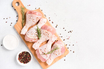 Raw chicken drumsticks with seasonings on wooden cutting board over white concrete background with copy space. Chicken legs ready to cook. Organic meat, healthy eating