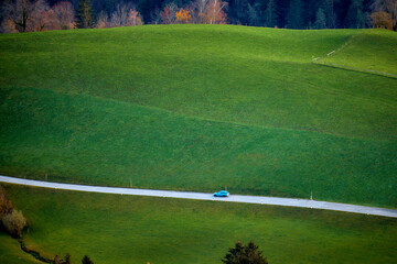 Ein Auto fährt auf einer Landstrasse umgeben von grünen Wiesen