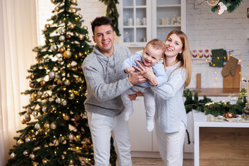 A happy family. Happy young couple with their little son in the kitchen decorated for the new year. New Year's interior in the kitchen. Christmas kitchen. Festive family atmosphere.