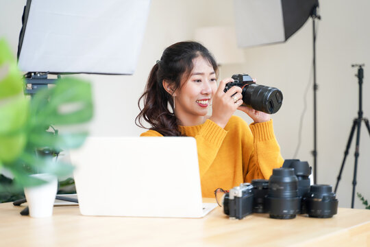 Lifestyle Asia young women photographer and freelance holding a dslr camera in  home office.  Female photographer smiling cheerfully working new project in studio