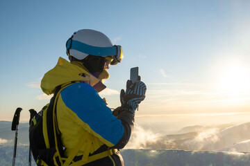 woman skier taking picture of sunset above the mountains