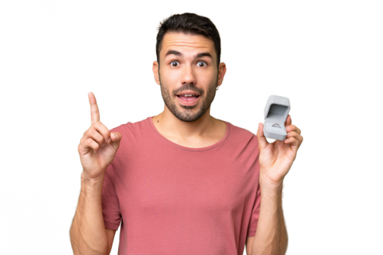 Young handsome caucasian man holding a engagement ring over isolated background pointing up a great idea