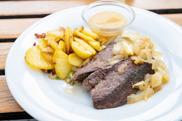 Fried calf liver with braised onions, roasted potatoes and apple puree on a white plate, selected focus