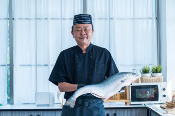 Portrait of cheerful chef standing with salmon fish. Chef cutting fish and making sashimi.