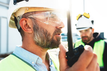 Portrait of bearded engineer wearing protect glasses and helmet use walkie-talkie on construction...