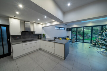 Stylish, modern, designer kitchen diner in white and grey with sofa/couch and beautiful garden showing through bifold doors. With Christmas/Xmas tree.