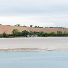 Sandy seashore. Calm water. The ship on the shore. A plowed field.