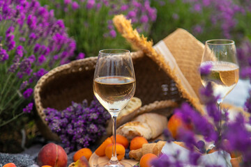 Wicker basket with delicious food for a romantic picnic in a lavender field. The girl pours wine.