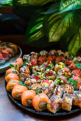 Big set of fresh japanese sushi rolls with tuna, sea bass, salmon, cucumber, avocado, cream cheese, mango, sesame, almond and green pea against background of flower leaves.