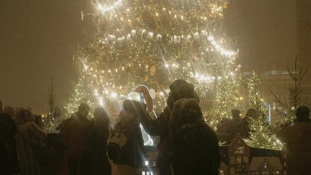 st. petersburg, winter 2022: People walks near the christmas tree in city, night time with a holiday illumination. tree with a decoration and garland. slow motion shot