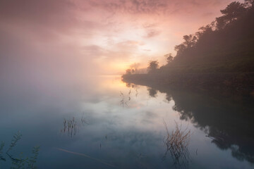 Fototapeta premium The water reflection of the sunrise breathtaking beauty nature scenery landscape with mountain mist in Khuean Phluang Reservoir nearby Khao Khitchakut National Park, Chanthaburi, Thailand 