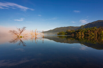 Fototapeta premium The water reflection of the sunrise breathtaking beauty nature scenery landscape with mountain mist in Khuean Phluang Reservoir nearby Khao Khitchakut National Park, Chanthaburi, Thailand 