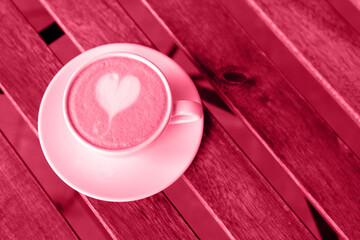 Viva Meganta toned red magenta cup of coffee on the wooden table near the street loft cafe. Barista heart shape sign on the cappuccino foam. Trendy color of the year 2023. Fashion color pattern

