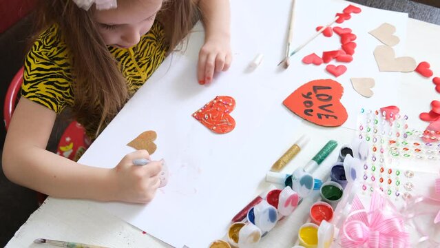 Child making homemade greeting card. A little girl paints a hearts as a gift for Mother’s Day or VAlentines day. Traditional play concept. Arts and crafts concept.
