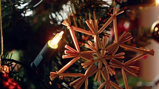 Ein Strohstern h&auml;ngt am Christbaum mit einer Lichterkette