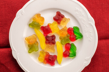 Several gummy bears on a white ceramic plate, macro, top view.
