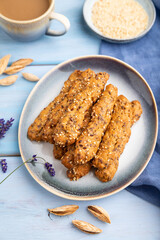 Crumble cookies with seasme and almonds on ceramic plate with cup of coffee on blue wooden background. side view, close up, selective focus.