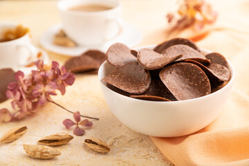 Chocolate chips with cup of coffee on a beige concrete background. side view, close up, selective focus.