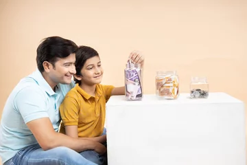 Fotobehang Saving Money and Investing Concept Happy Young Indian Father and Son Put Rupee Notes Or Cash In Multiple Glass Jar Bottles Isolated On Beige Studio Background. © gajendra