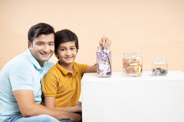 Saving Money and Investing Concept Happy Young Indian Father and Son Put Rupee Notes Or Cash In...