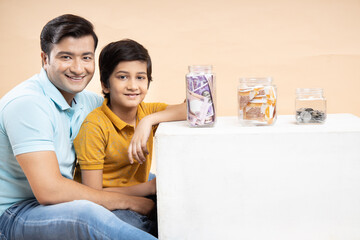 Saving Money and Investing Concept Happy Young Indian Father and Son Put Rupee Notes Or Cash In...