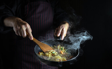 Cooking fresh vegetables and noodles. The chef flips food in a hot frying pan. Space for recipe or menu on black background - obrazy, fototapety, plakaty