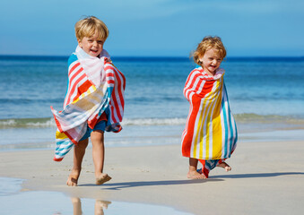 Children boy, girl covered in towel run after swim on beach