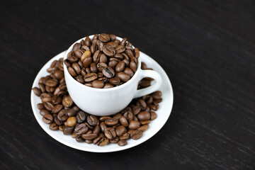 Coffee beans in white cup on dark wooden table. Dark and roasted coffee, concept of natural drink