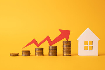 Coins on a table, a red up arrow and house. The concept of the rising price of real estate