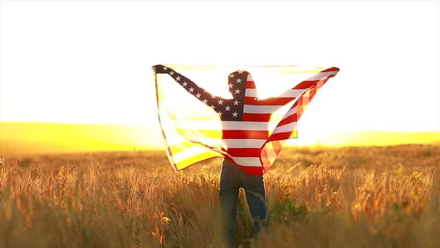 woman in field holding USA stars and stripes flag in golden sunset evening sunshine.