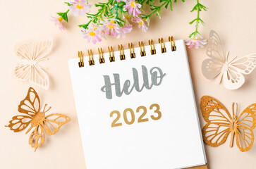 The Hello 2023 calendar desk for the organizer to plan and paper butterfly with flower on yellow background.