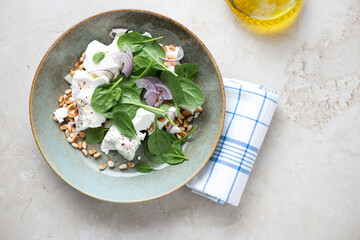 Rustic plate with fresh spinach, pine nuts and feta salad, horizontal shot on a beige stone background, above view with space