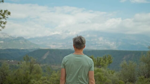 rear view inspired man walking outdoors on mountains background and rising His Arms. man traveler enjoying beauty of nature and wilderness outdoors in Turkey. Travel vacation concept
