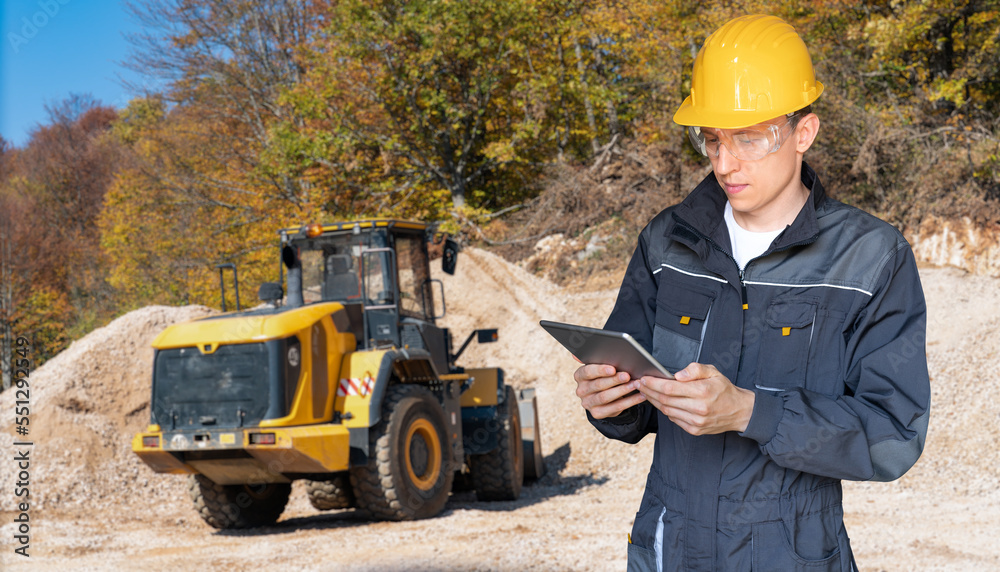 Poster Engineer in a helmet with a digital tablet on the background of construction machine	