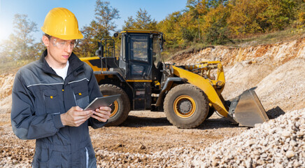 Engineer in a helmet with a digital tablet on the background of construction machine	