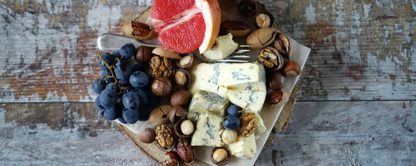 Cheeseboard. Cheese with nuts, grapefruit and grapes on a wooden board. Healthy snacks.