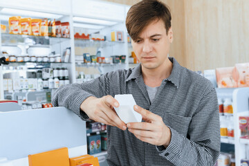Young thoughtful caucasian man reading medicine, medical label product before decide buying from...