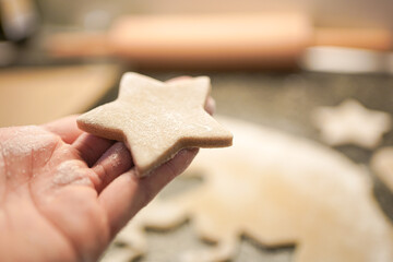 hand holding a star-shaped christmas cookie cut out of gingerbread dough. 