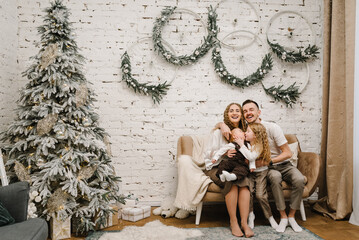 Father, mother hugs son and daughter on sofa near Christmas tree at home. Mom, dad with kids. Happy New Year and Merry Christmas. Christmas decorated interior. The concept of family holiday. Close up.