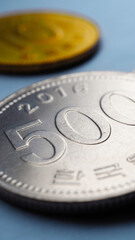 Translation: Bank of Korea. Korean coins lie on blue paper surface. 500 won coin close-up. Vertical stories illustration about economy, finance or bank. Money and business in South Korea. Macro