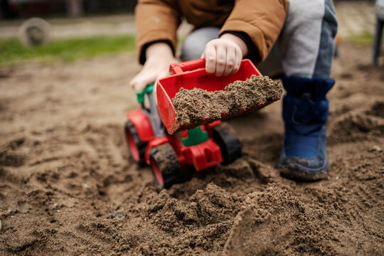 Cropped picture of a boy playing in sand with excavator toy.