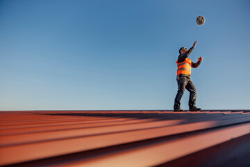 A construction worker is playing with helmet while standing on the roof.
