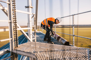 A metal construction worker is relocating rusty pipe while standing on height.