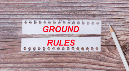 Background for text. White strips of paper with the text GROUND RULES and a white pencil next to it on a wooden background