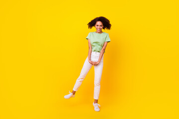 Fototapeta na wymiar Full body length photo of young adorable gorgeous nice girl wear green t-shirt white pants staying tiptoes shy hands dance isolated on yellow color background