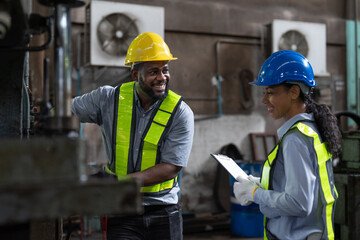 Happy African American male and female engineers in safety vest and helmet working at heavy metal industrial factory. Two technician foreman discussing for checking and repairing machine at factory.